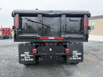 Ford F750 dump truck rear showing dual mud flaps with contact numbers, tailgate, and bumper lights.