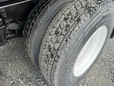 Ford F750 dump truck front wheel and tire close-up, dual rear axle, muddy tread on tire.
