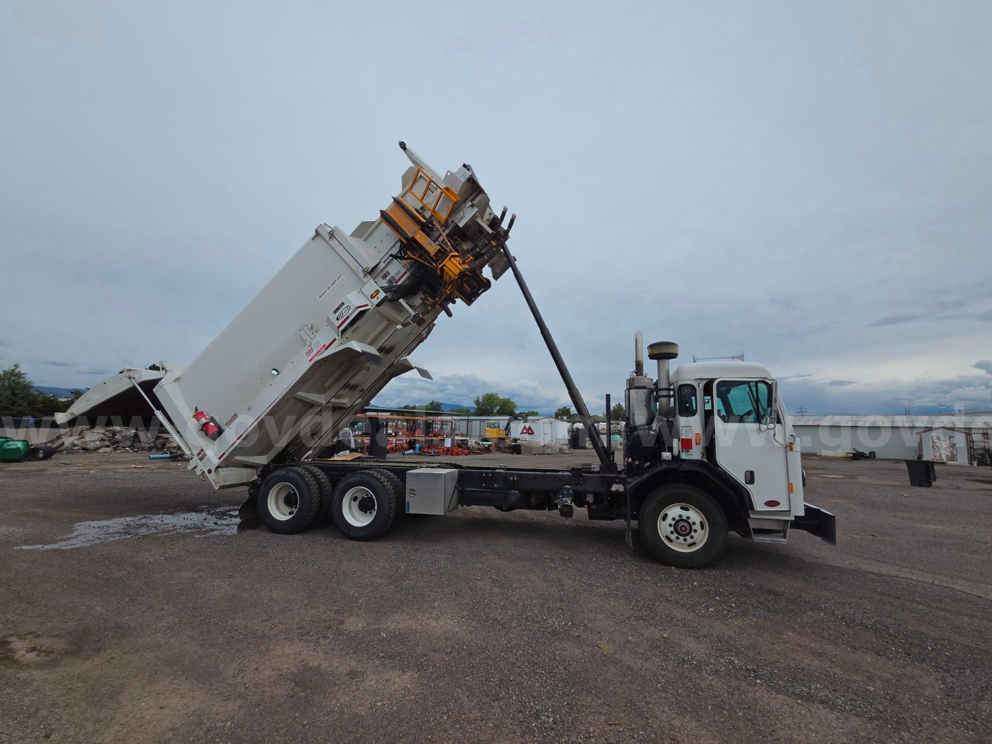 Truck in yard with a dump body raised for unloading, Peterbilt cab, dump bed and hoist visible.