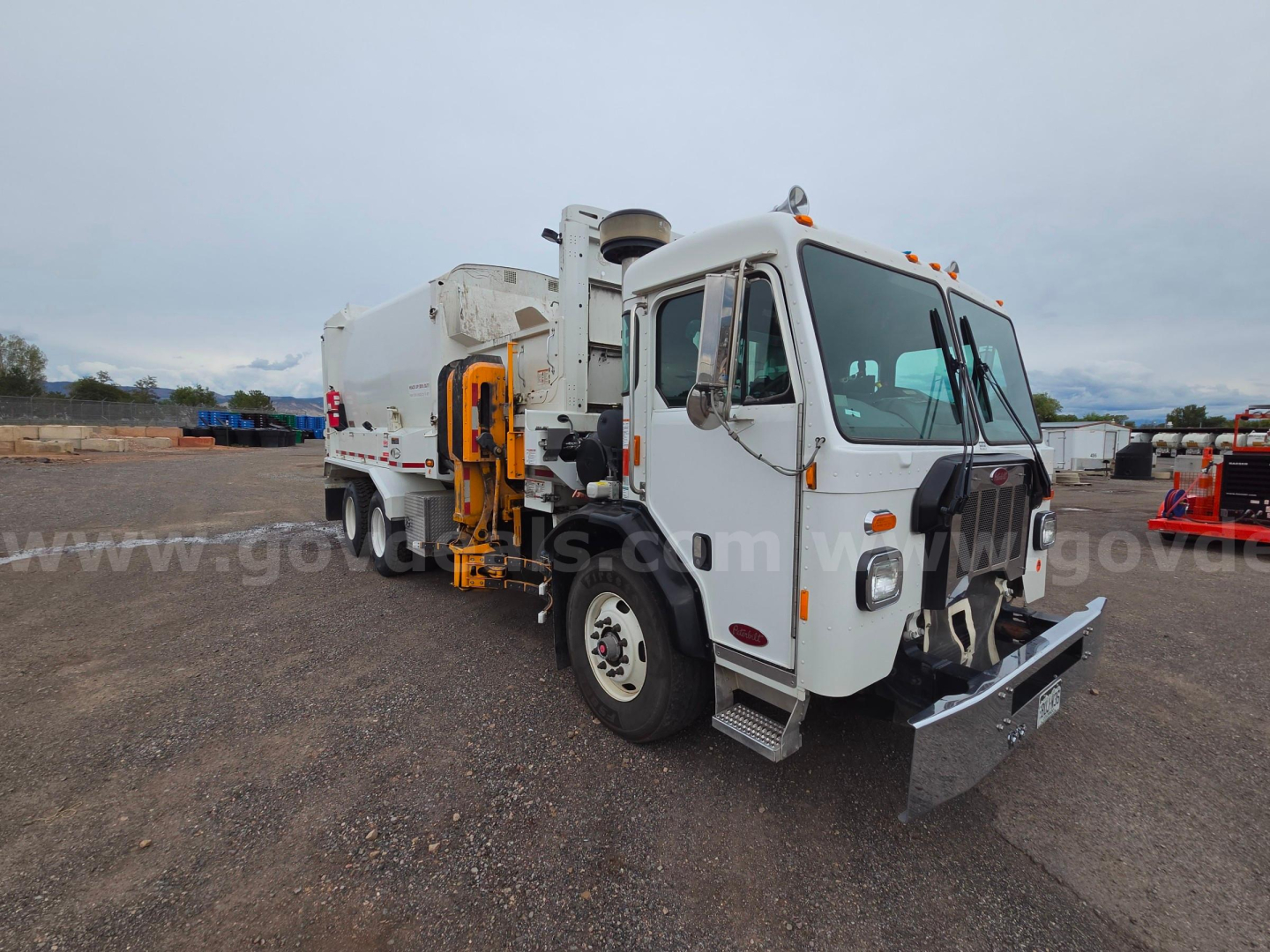 Peterbilt 520 truck in a gravel lot, white cab, utility body, front bumper with metal plow, side mirrors, amber roof lights, used condition.