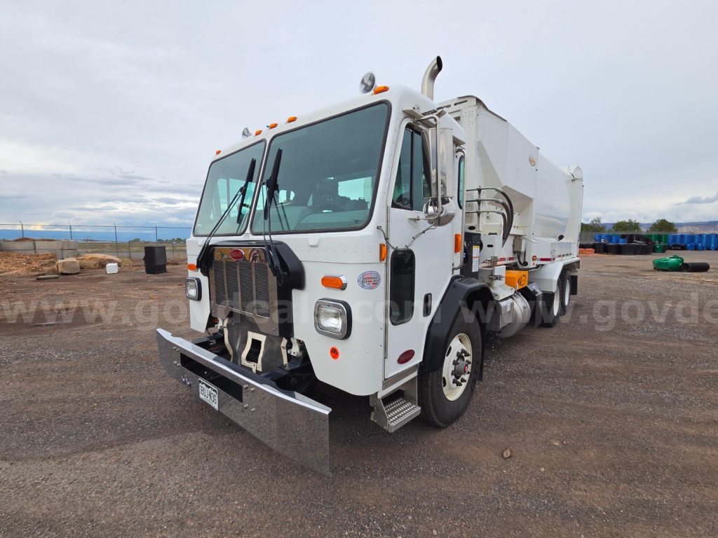 Peterbilt 520 dump truck front-left angle showing plow, cab, grille, headlights, and side mirrors.