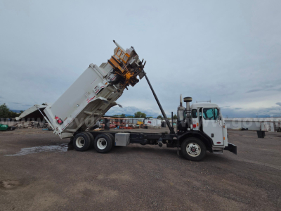 Truck in yard with a dump body raised for unloading, Peterbilt cab, dump bed and hoist visible.