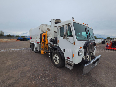 Peterbilt 520 truck in a gravel lot, white cab, utility body, front bumper with metal plow, side mirrors, amber roof lights, used condition.