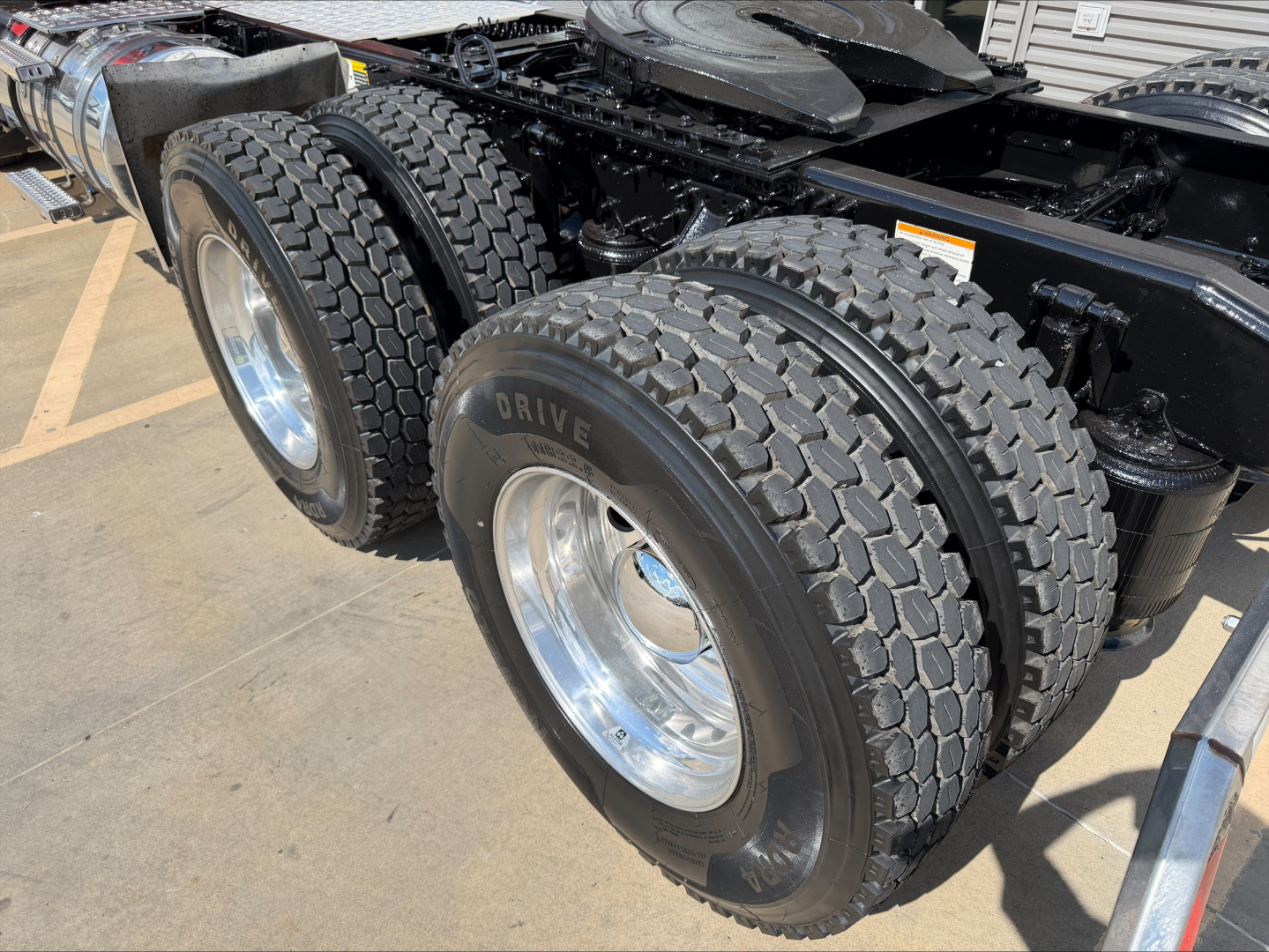 Truck axle region with dual rear wheels and heavy-duty tires; chassis and suspension visible under a 2022 Mack Anthem cab.