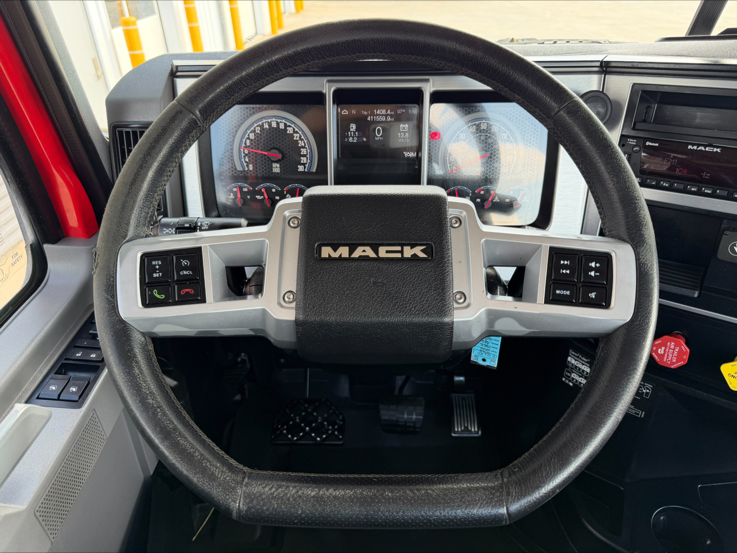 Mack truck cockpit showing steering wheel with 'MACK' center emblem and instrument cluster.