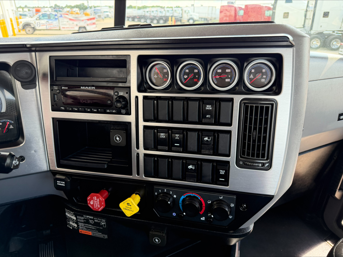Mack Anthem dash cluster showing gauges, stereo, push buttons, climate controls, and red/ yellow hazard knobs.