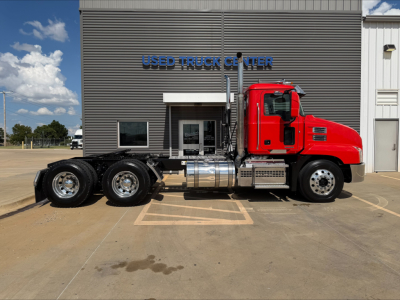 2022 Mack Anthem conventional daycab truck side view showing red cab, chrome fuel tanks, and dual rear axles in front of used truck center.