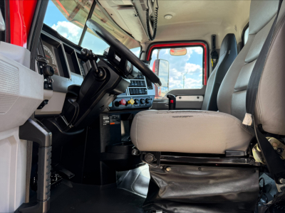 Mack Anthem truck interior view showing steering wheel, dashboard gauges, center console, and driver seat with light gray upholstery