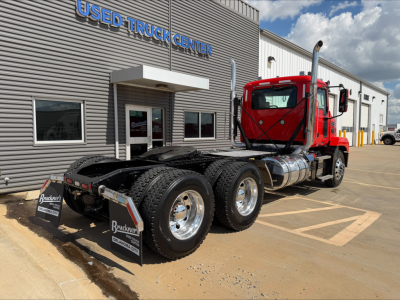 Mack Anthem tractor on lot facing camera, red cab, dual rear axles, fuel tanks, and chrome wheels beside Used Truck Center building.