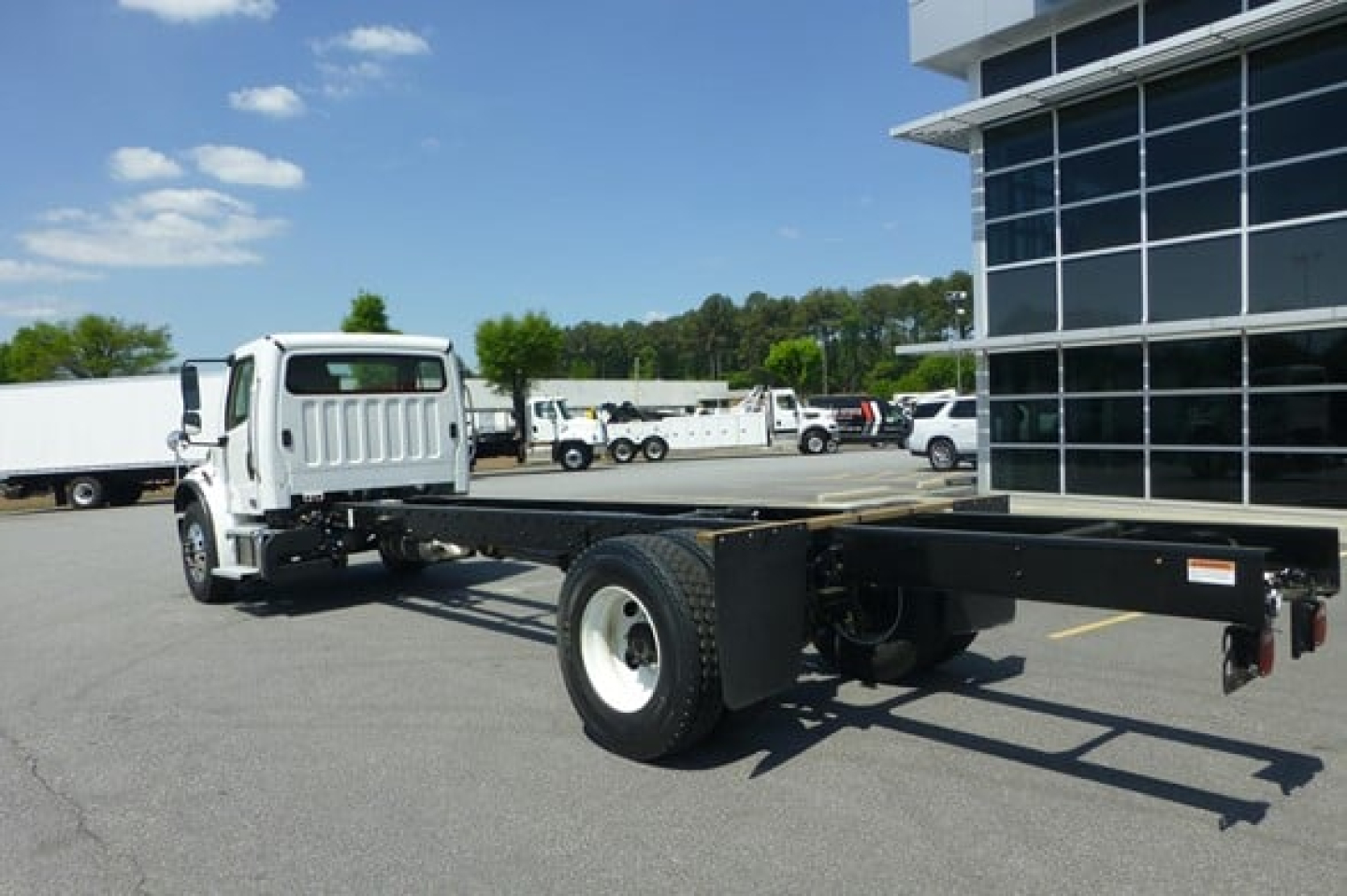 Freightliner M2 106 Plus cab and chassis truck in dealership lot, side view showing long frame and single rear axle