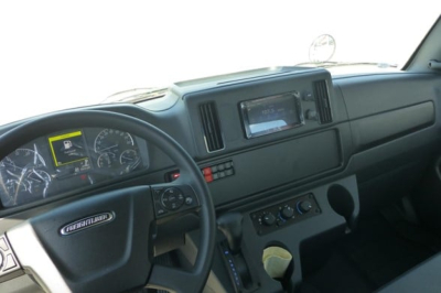 Freightliner M2 106 Plus cab interior showing steering wheel, dashboard gauges, center console, and infotainment screen.