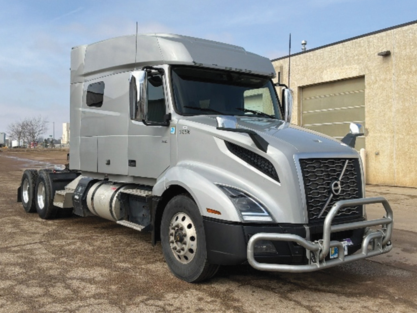 Volvo VNL 740 sleeper cab tractor truck in a light silver color, front grille with bull bar, side view showing dual rear axles, large fuel tanks, and aerodynamic mirrors.