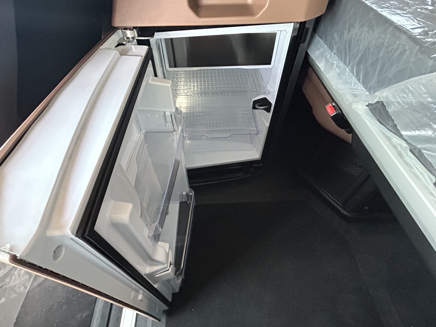 Mini fridge with open door in cabin showing empty shelves and freezer, mounted under countertop.