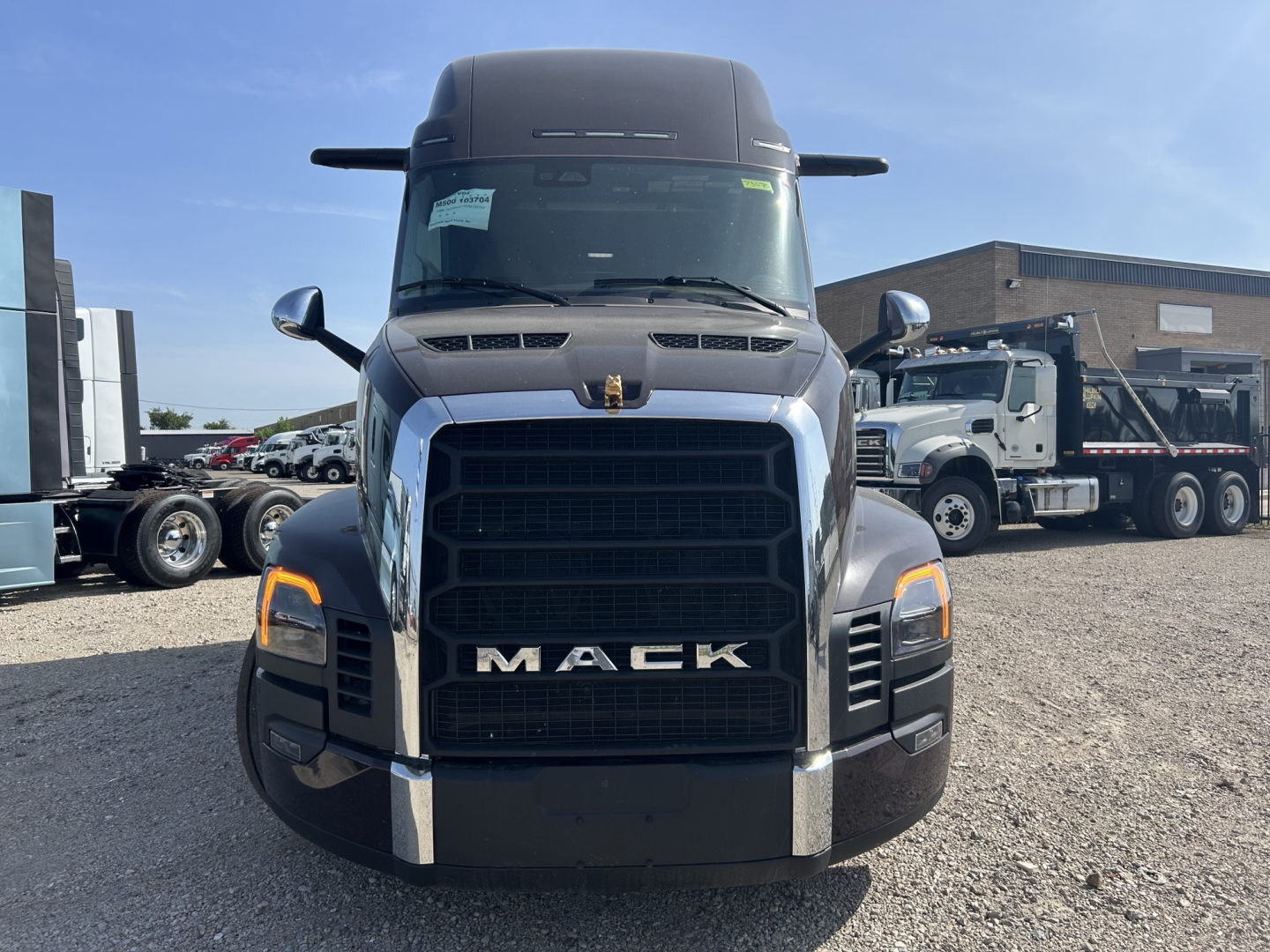 Mack PR64T76H truck front view showing large black grille with MACK lettering, headlights, and chrome bumper.