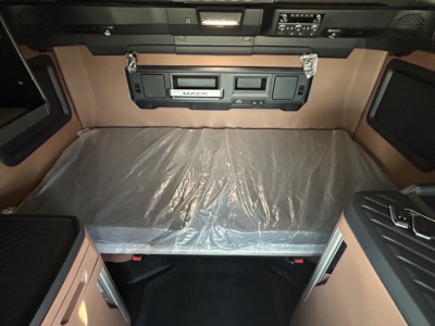 Truck cab interior of a Mack PR64T76H showing sleeper bed with plastic cover, overhead controls, and storage compartments.