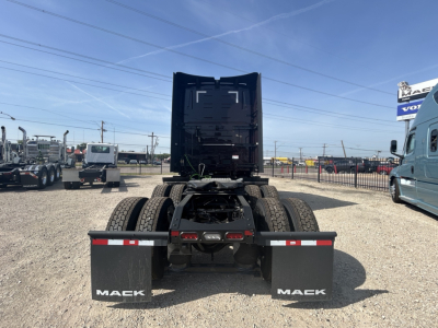 Rear view of a Mack truck tractor with dual rear axles and fuel/air lines visible, mud flaps labeled MACK, fifth wheel area obscured, clear sky.