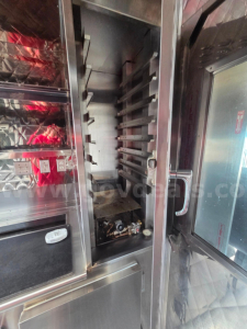 Catering truck interior with vertical rack slots and metal panels; empty knife racks and stainless steel surfaces.