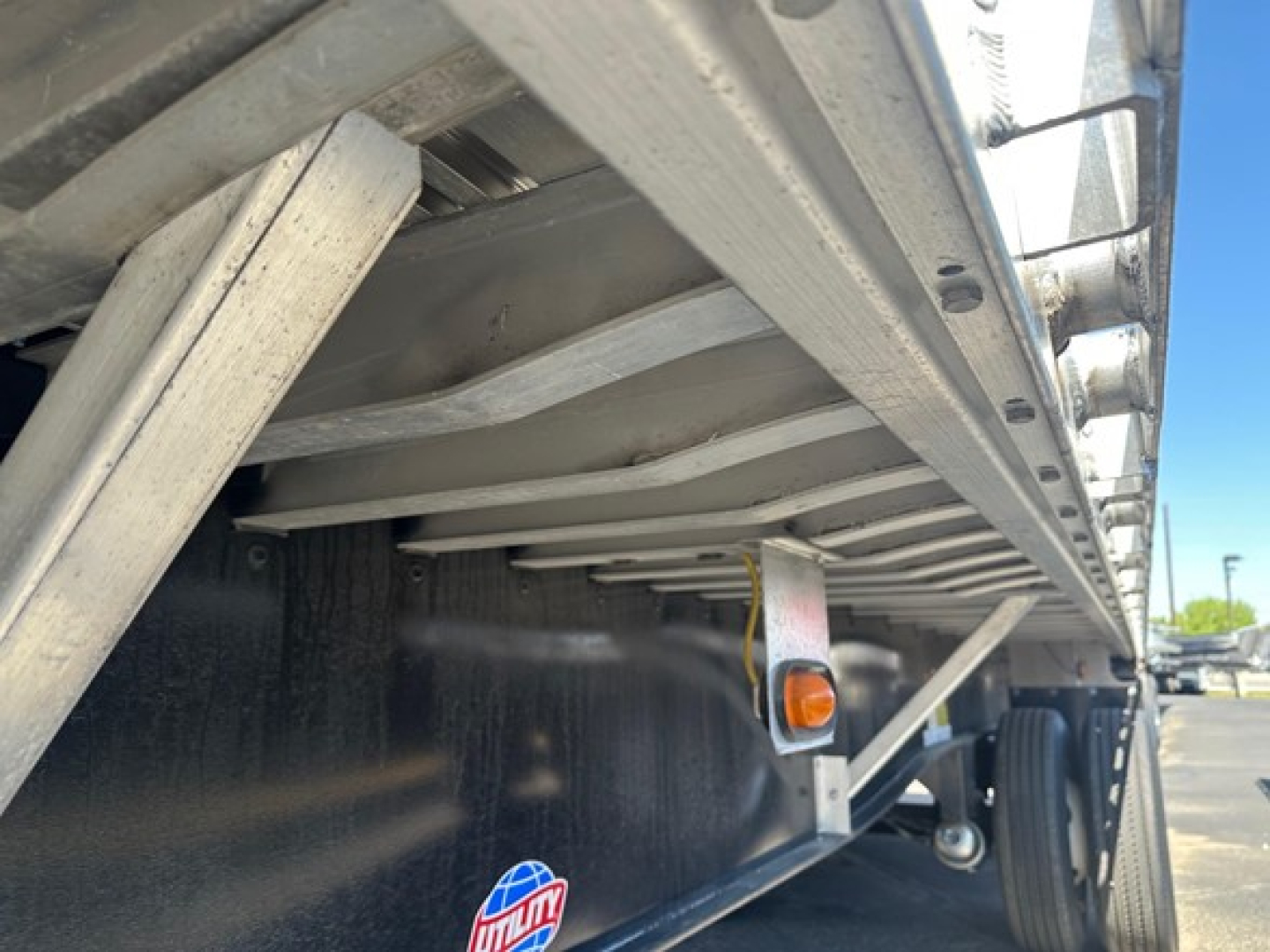 Trailer side view showing underside frame and wheel area of a 2024 Utility 48' spread air combo flatbed; visible components include the steel frame, cross members, and a marker light.