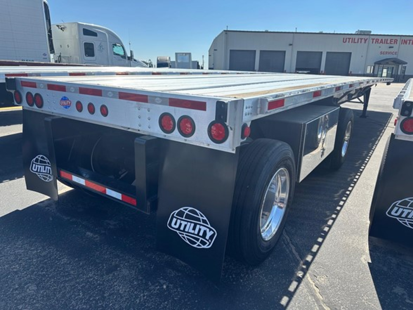 Flatbed trailer rear view showing dual axles with Utility mud flaps and red/white reflective tape along edges.