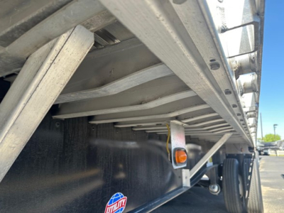 Trailer side view showing underside frame and wheel area of a 2024 Utility 48' spread air combo flatbed; visible components include the steel frame, cross members, and a marker light.