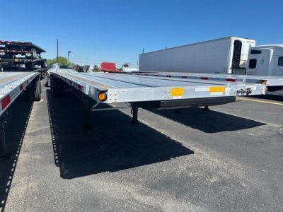 Flatbed trailer with a 48' spread air combo; metal frame, dual axles visible, reflective markers along sides, dealership lot in background.
