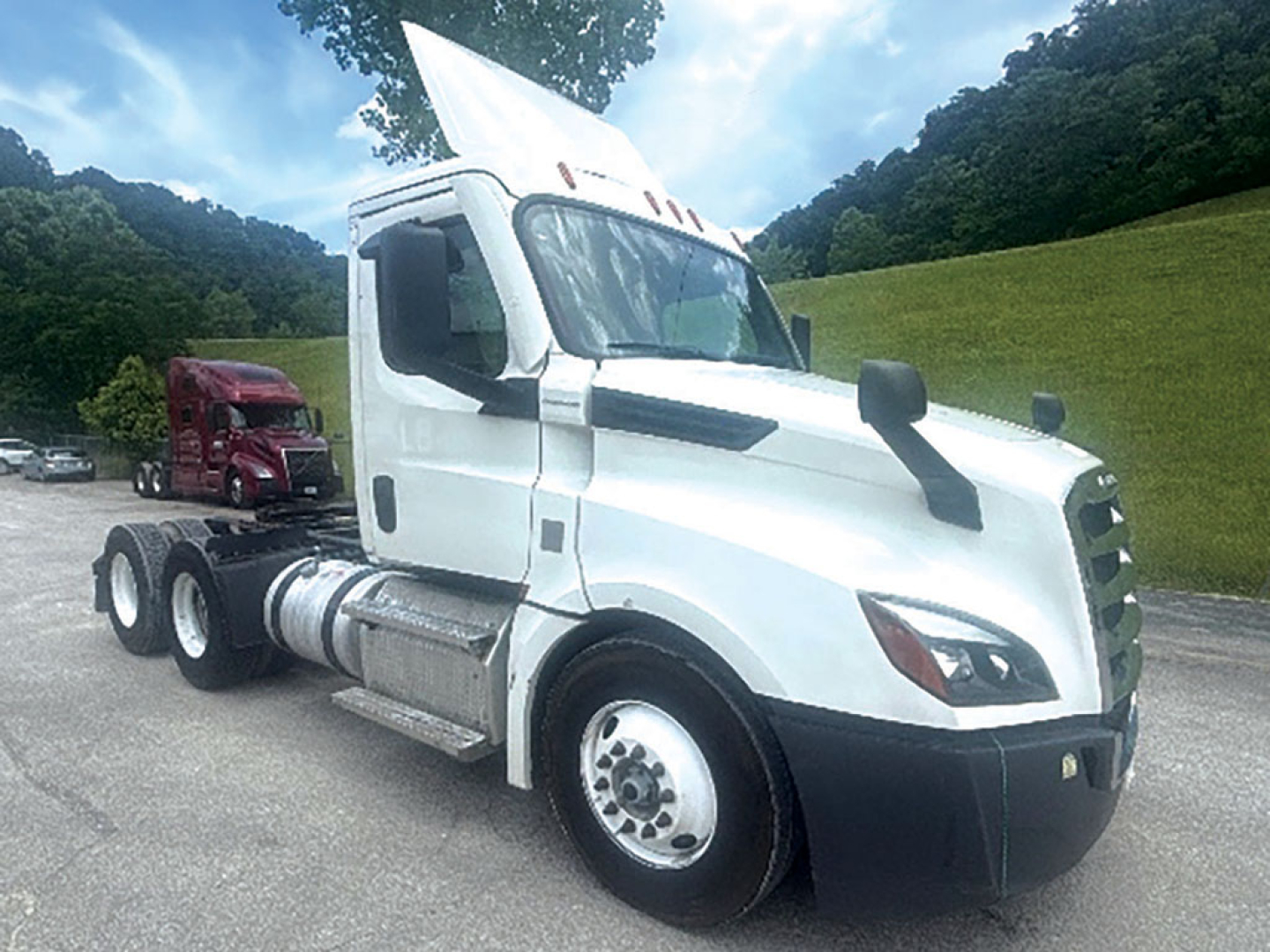 Truck cab with white Freightliner Cascadia in sidelong view; visible text includes DOT-style stickers and vehicle details on the side and front, no clear serials readable.