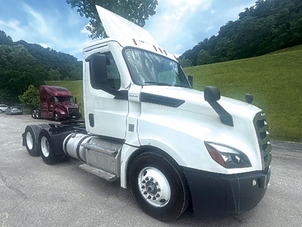 Truck cab with white Freightliner Cascadia in sidelong view; visible text includes DOT-style stickers and vehicle details on the side and front, no clear serials readable.
