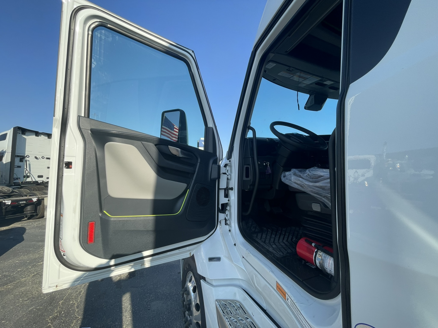 Truck cab interior entry door open showing steering wheel and driver seat area of a Volvo VNL64T860 truck, with light gray interior and black floor mats.