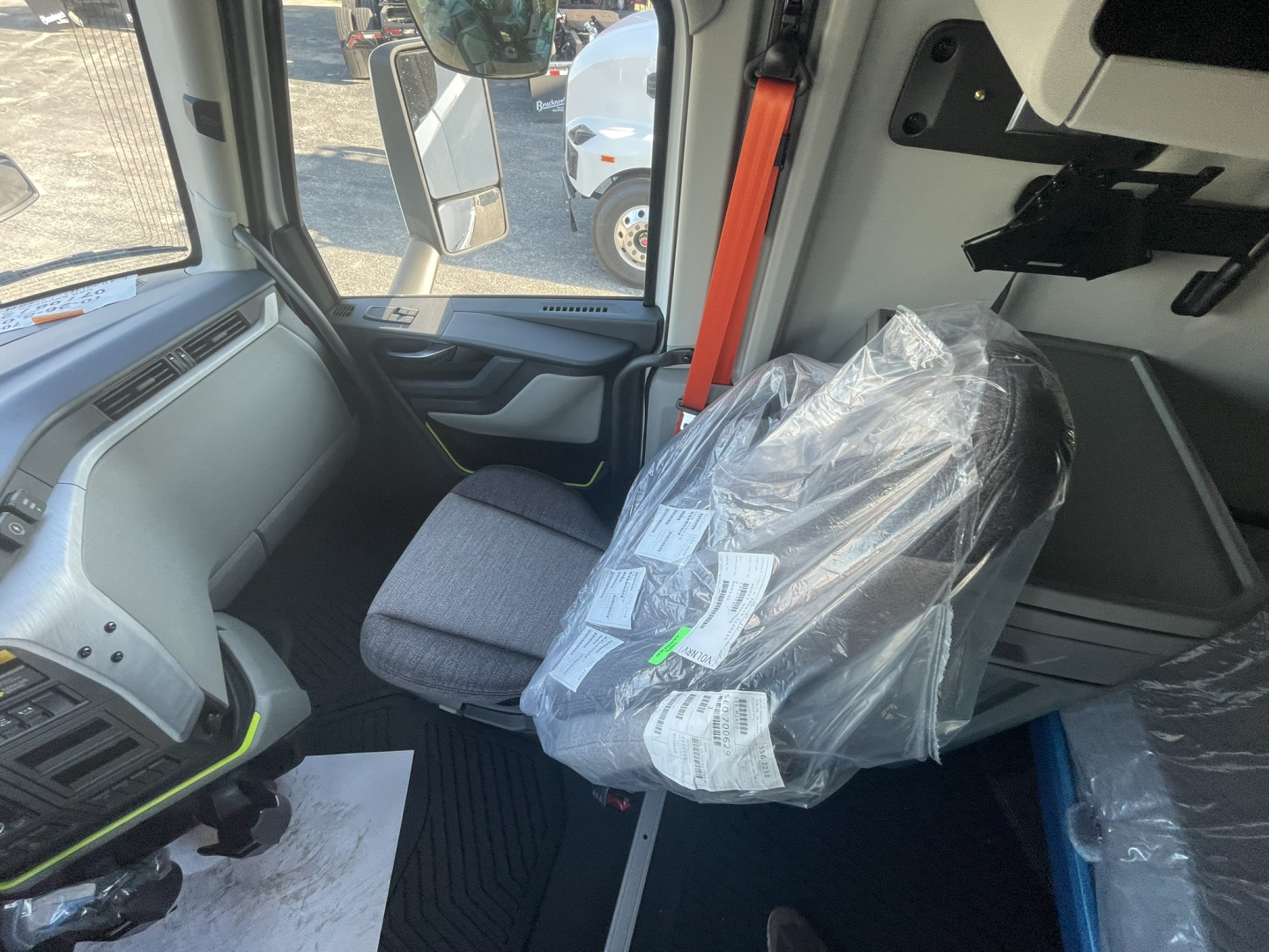 Cab interior of a Volvo VNL64T860 tractor showing driver seat with plastic-wrapped seat, dashboard, and door panel.