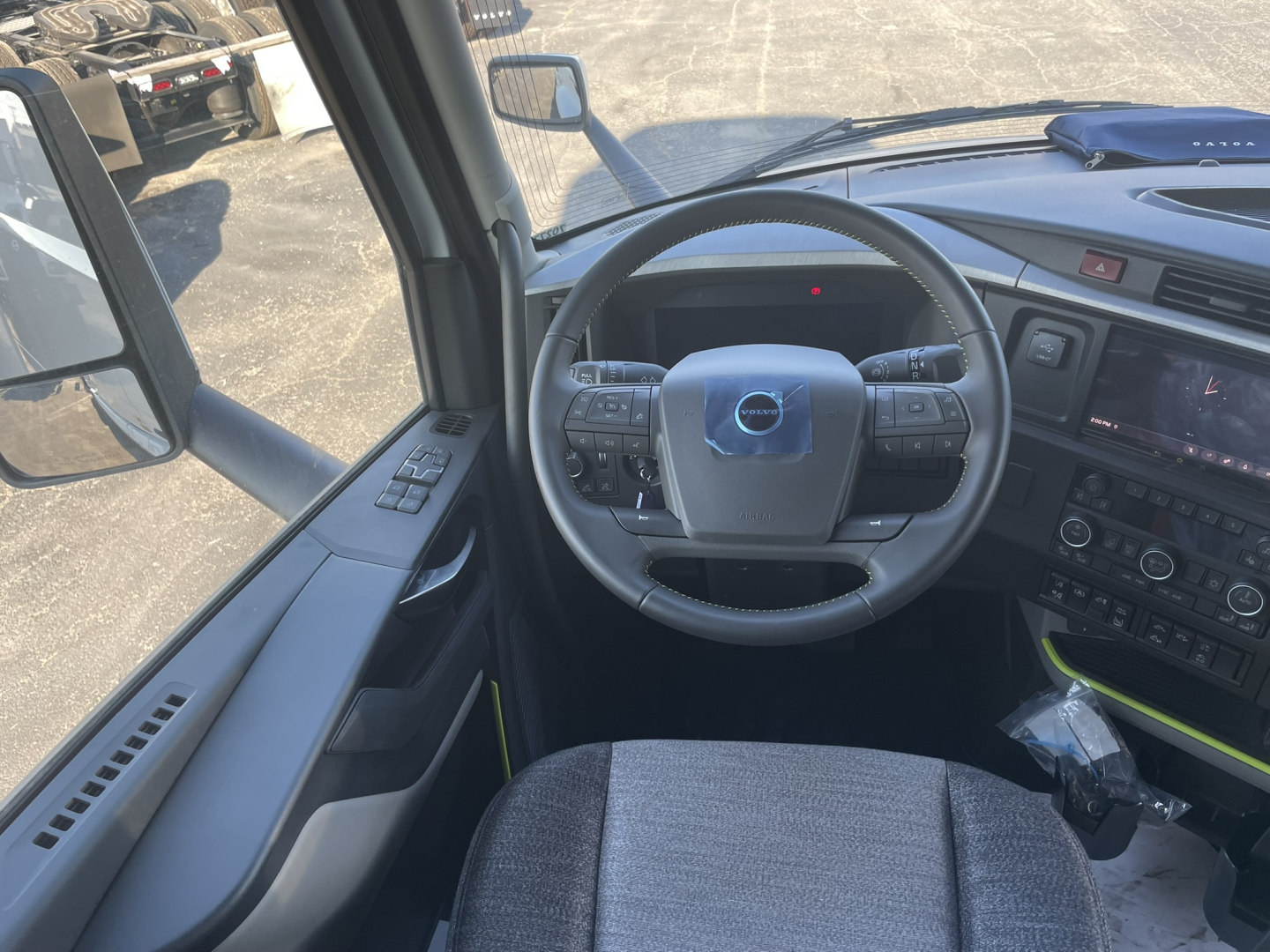 Volvo VNL64T860 cabin interior showing steering wheel with Volvo emblem, dashboard controls, and side door panel; front windshield and side mirror visible.