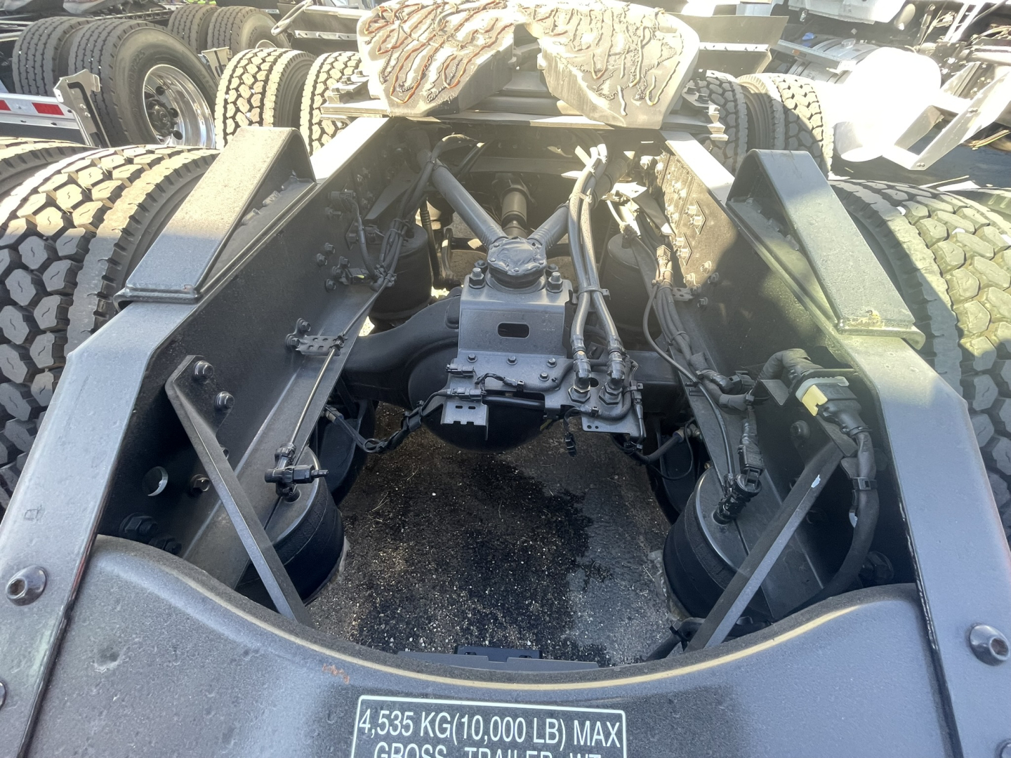 Truck chassis showing rear fifth-wheel mount and drivetrain with dual axles, tires, and suspension components; visible max weight label 4,35 KG(10,000 LB) MAX.