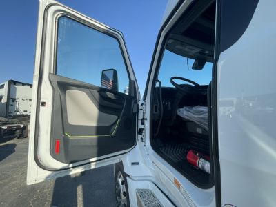 Truck cab interior entry door open showing steering wheel and driver seat area of a Volvo VNL64T860 truck, with light gray interior and black floor mats.