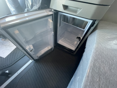 Volvo VNL64T860 cab interior showing open under-counter fridge/freezer with empty shelves; compact kitchenette area near driver seat.