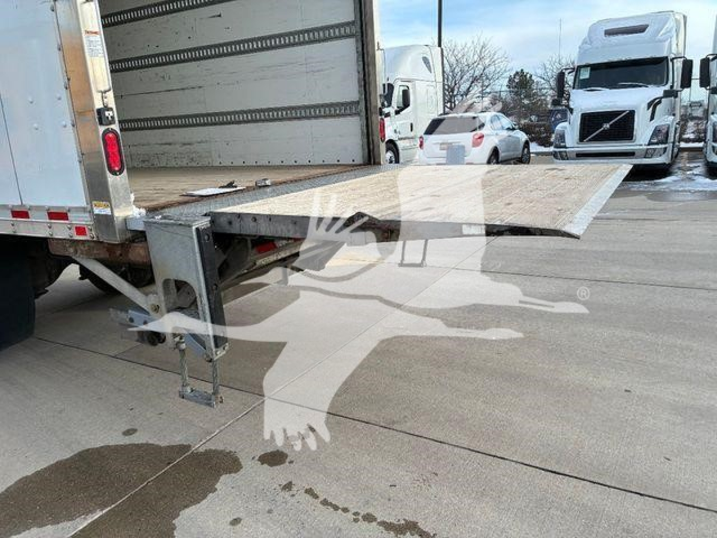 Truck rear with a loading ramp extended from a box truck bed, platform and hydraulic support visible.