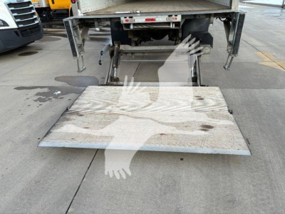 Truck rear with loading ramp deployed; metal ramp platform shows surface marks. Part of chassis and hydraulic mechanism visible beneath and behind. 