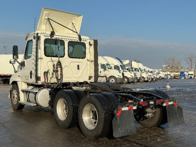 Truck chassis and cab of a Freightliner Cascadia125 with dual rear axles and raised hood, row of similar trucks in the background.