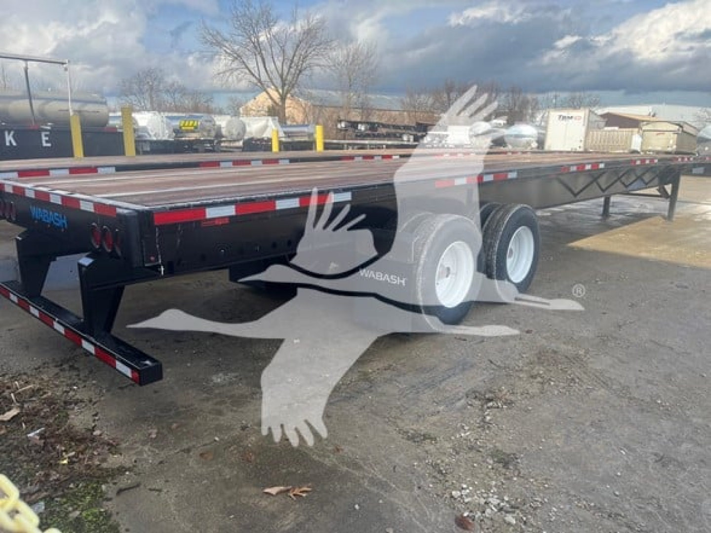 Flatbed trailer showing dual rear axles and Wabash branding on the side; long flat deck with safety rails and rear markers visible.