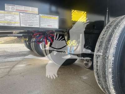 Trailer hitch area of a new Wabash flatbed trailer showing electrical cables and decals; warning labels and a yellow caution sticker are visible along the side; tires and undercarriage visible.