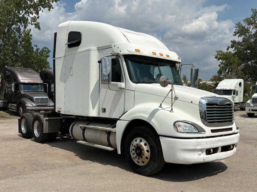 Truck cab and chassis of a 2013 Freightliner CL120 Columbia tractor in a lot, white cab with sleeper, large grille, dual rear axles, side fuel tanks.