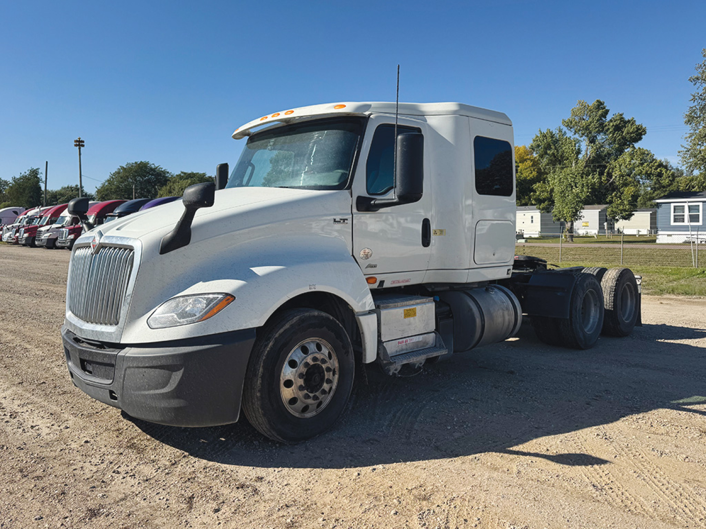 Truck cab and chassis of a white 2021 International LT625 conventional sleeper, side view showing front wheel, fuel tanks, and fifth wheel area.