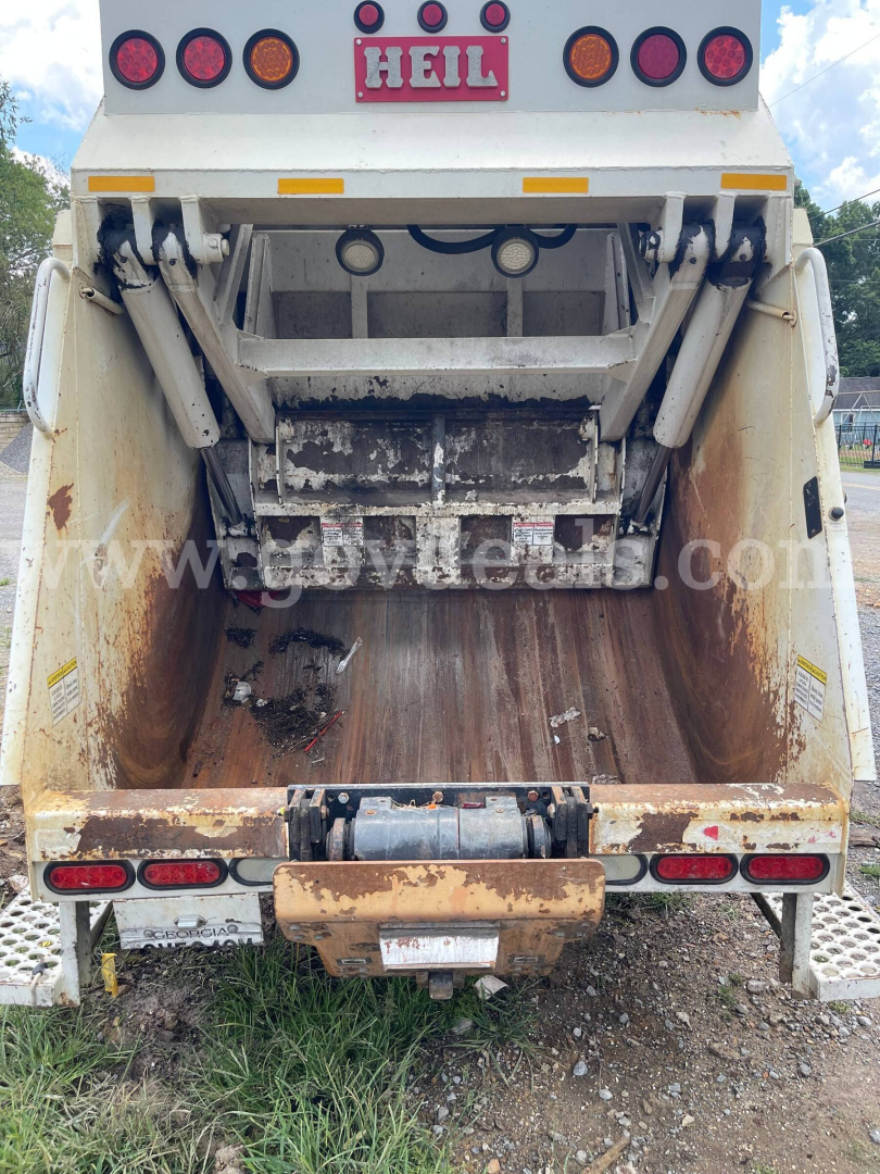 Back of a 2019 Hino 195 dump truck bed with hydraulic components and dirt in the chute, taillights, and Hell logo plate visible.