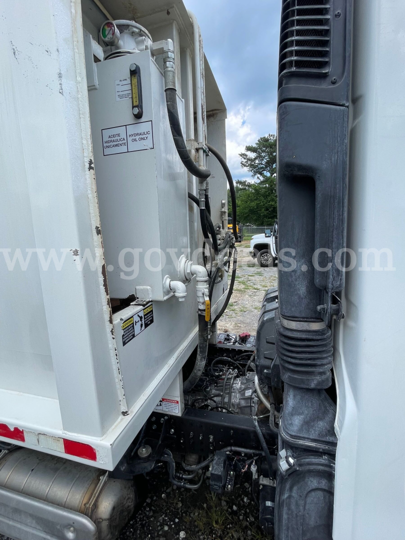 Truck engine bay of a 2019 Hino 195 showing coolant reservoir and hydraulic lines with warning labels.