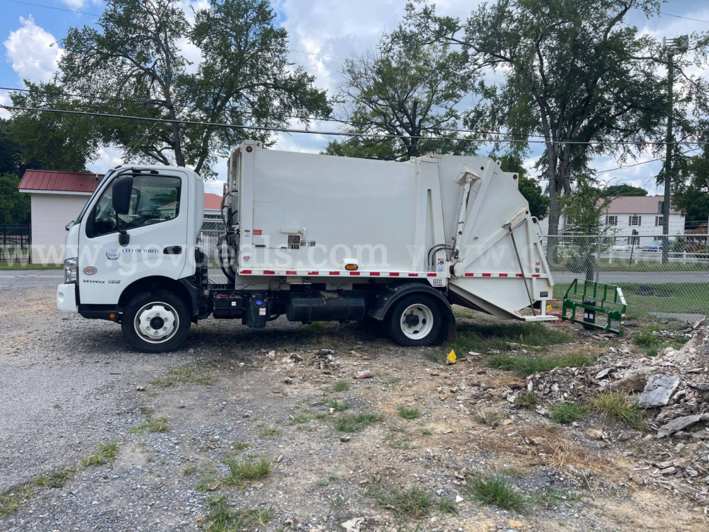 Garbage truck side view 2019 Hino 195 with rear compactor, white body, cab, and hydraulic lifting mechanism visible.