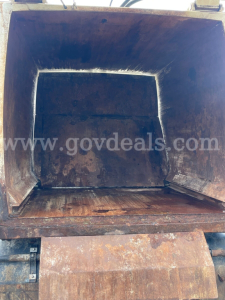 Dump truck bed interior showing rust and wear with open tailgate, cargo area empty.