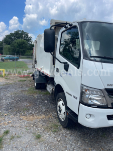 Garbage truck front cab and side showing Hino branding and wheel fender.