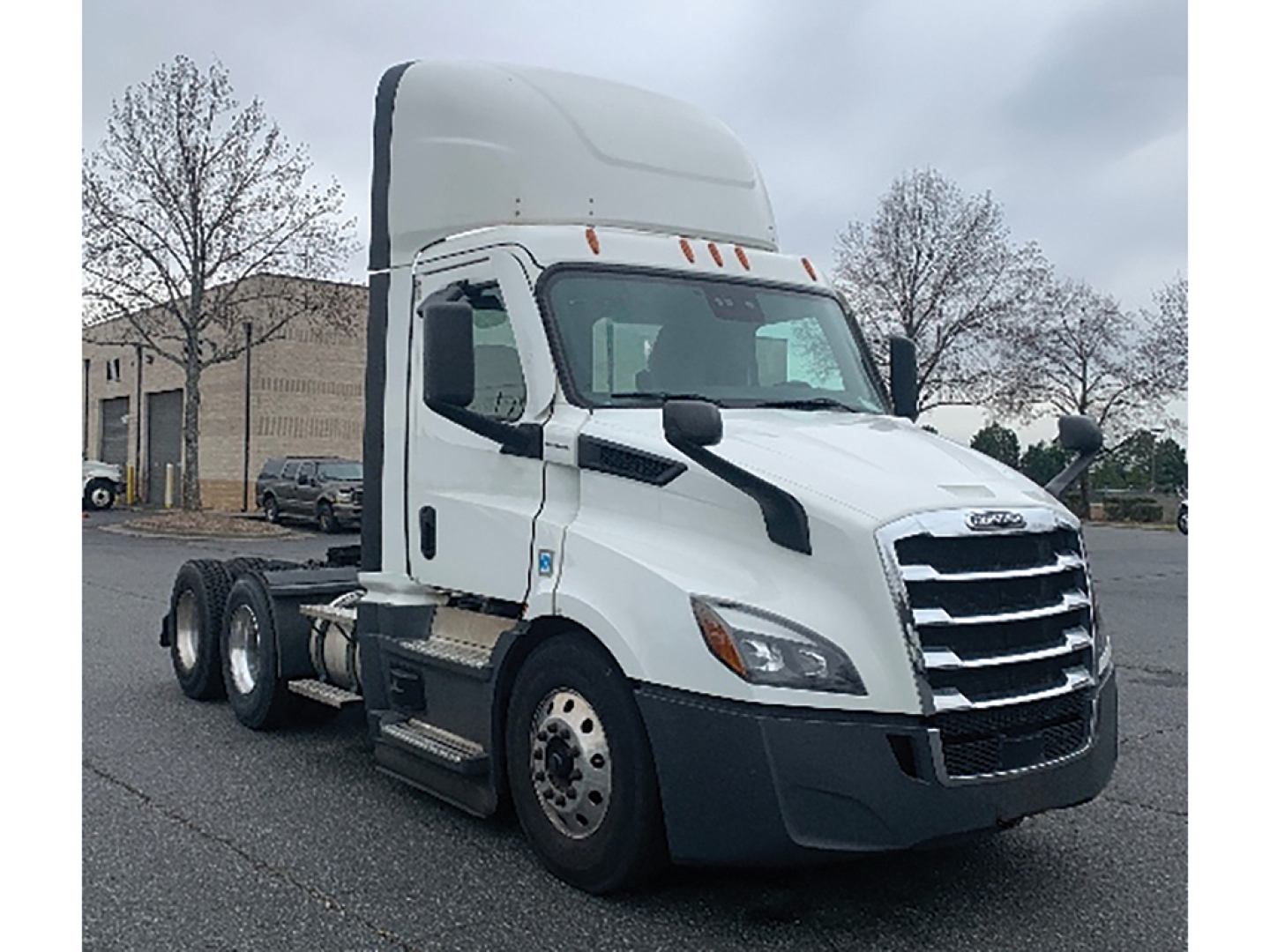 Truck cab from a Freightliner Cascadia showing front grille and side mirror in a parking lot.