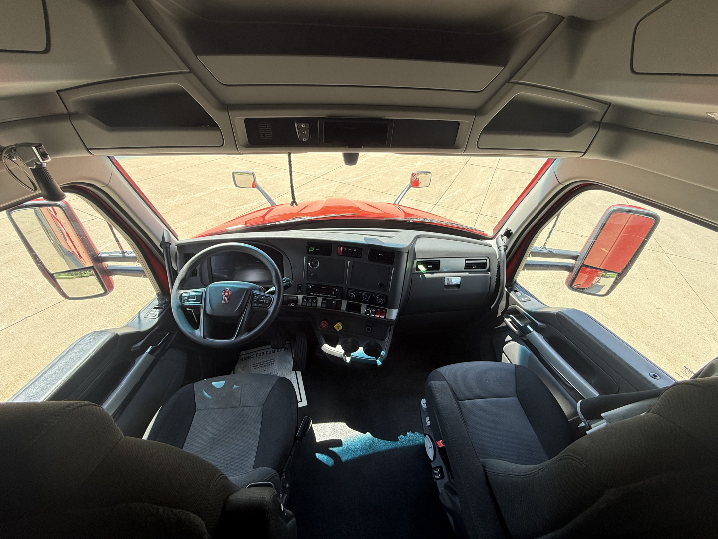 Kenworth T680 interior cab view from front seats showing dashboard, steering wheel, and side mirrors.