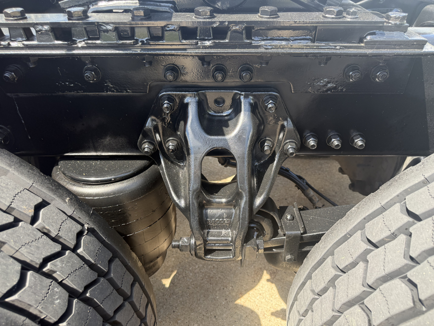 Kenworth T680 rear view showing suspension and drivetrain with visible leaf springs and universal joint, undercarriage components visible.