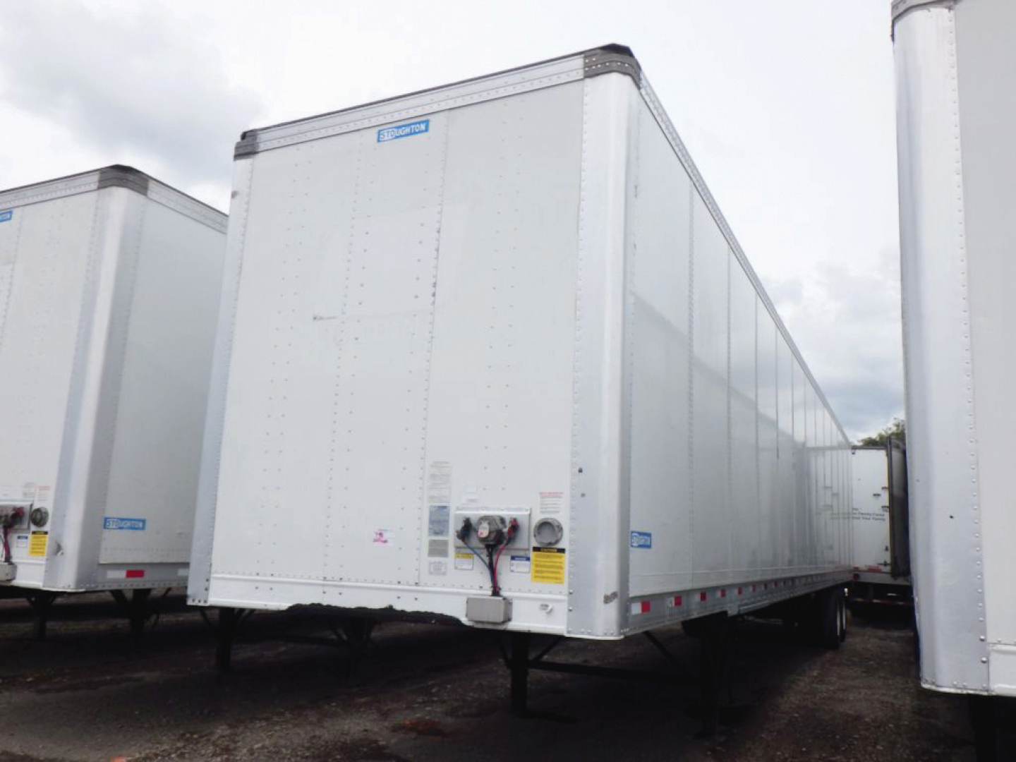 Stoughton plate van trailer with front view, shiny silver exterior, VIN tag and safety stickers visible on nose in a trailer yard.
