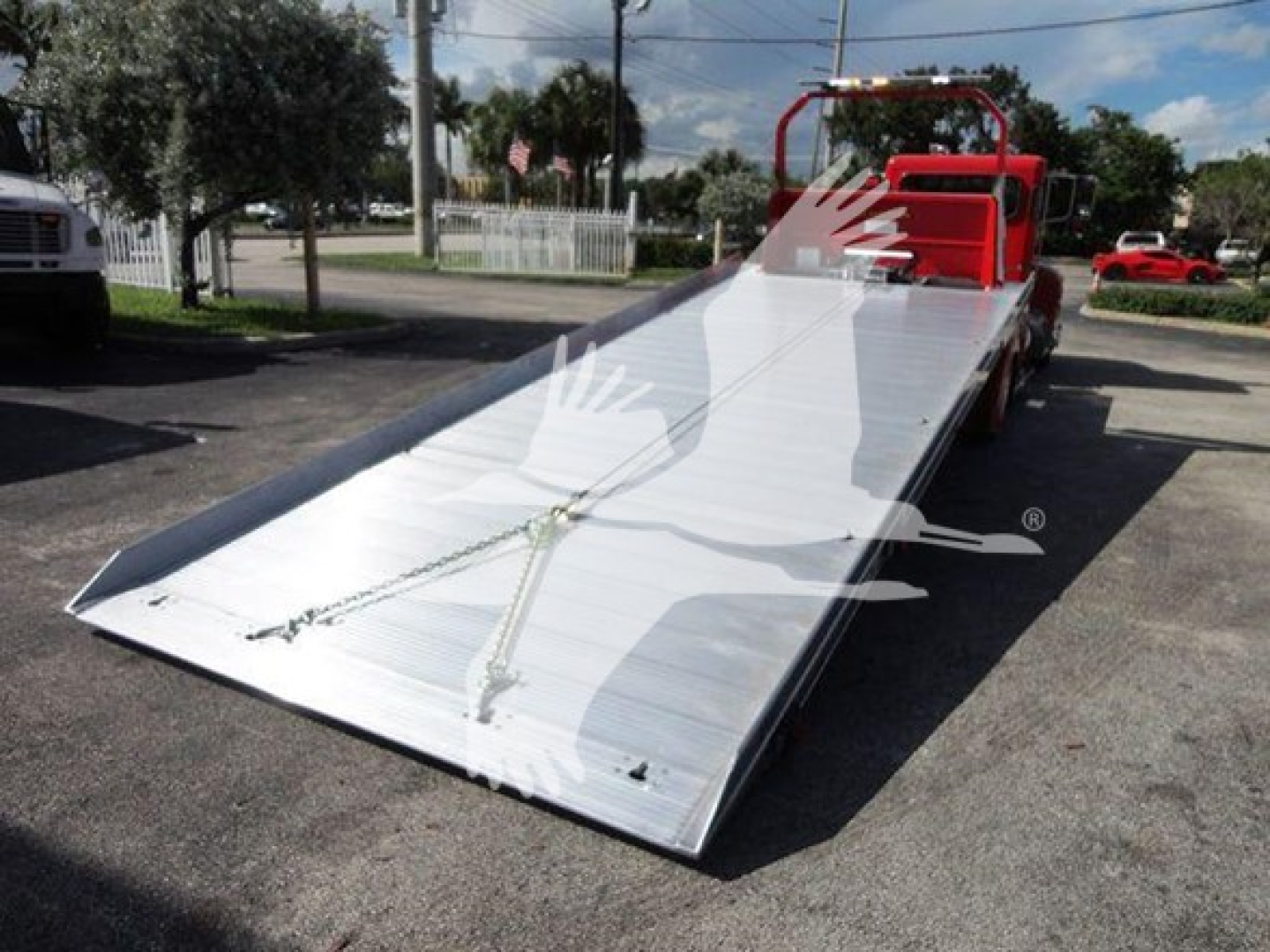 Peterbilt 337 rollback tow truck with a lowered aluminum ramp bed, red cab section visible, outdoor lot.